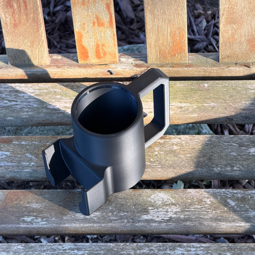 The empty black mug-style holder seen from above, showing the open can well, the square handle and the front pouch pocket