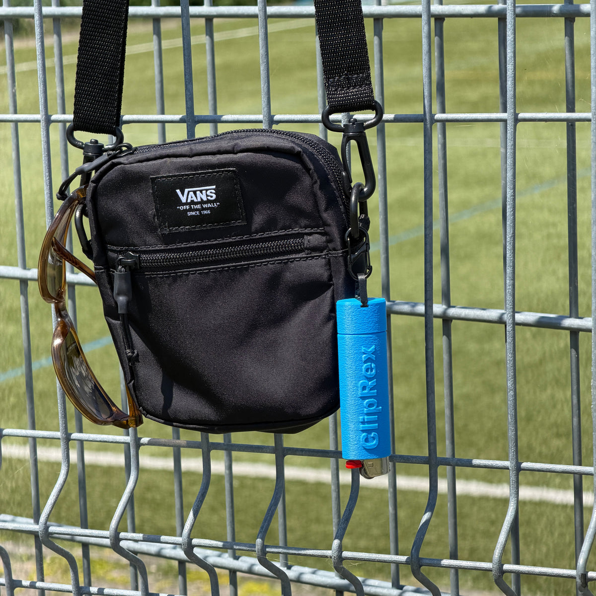 Blue ClipRex lighter holder clipped to the strap of a black crossbody bag